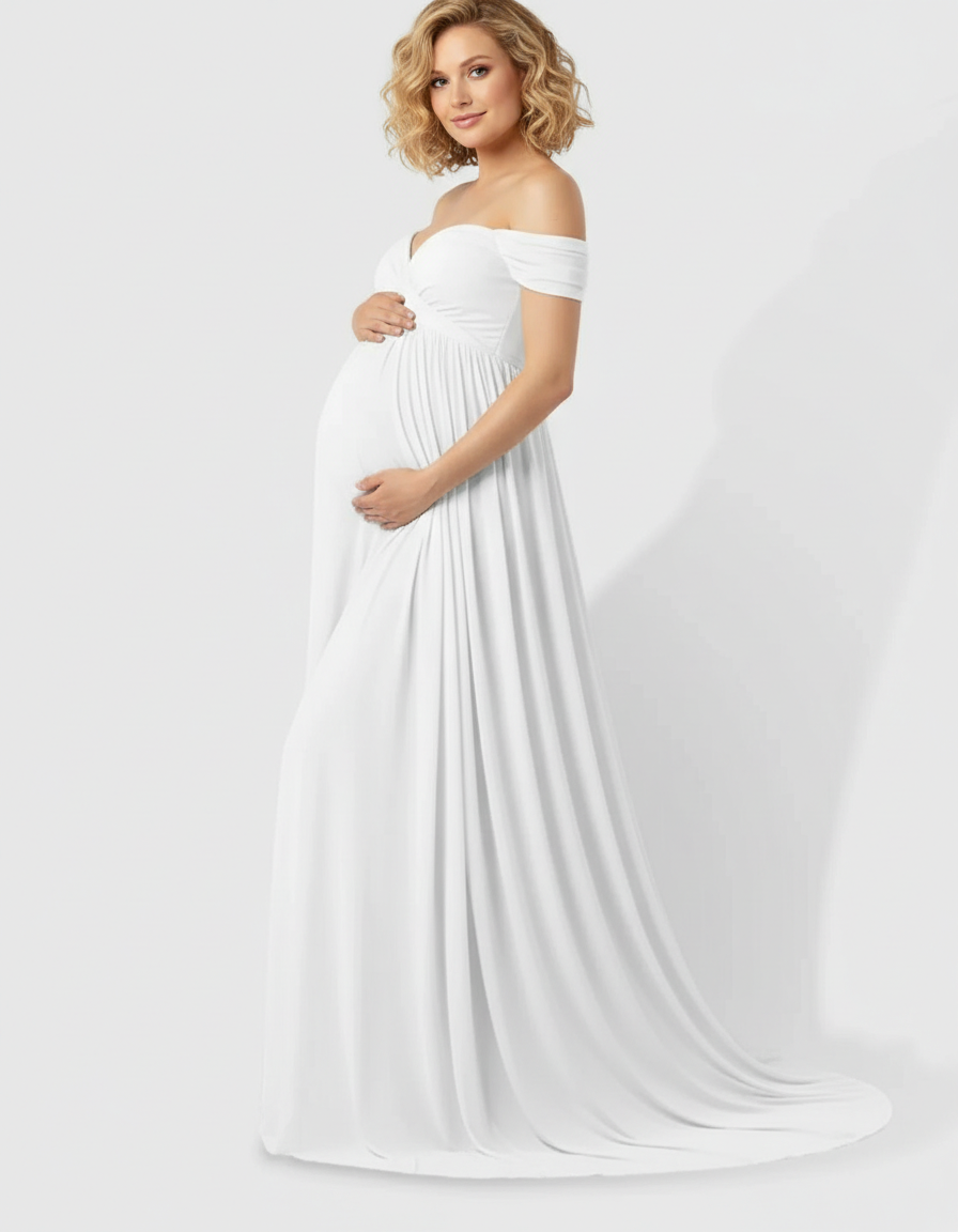 Blonde pregnant woman in a white off-shoulder laced flowing maternity maxi dress, holding her baby bump.