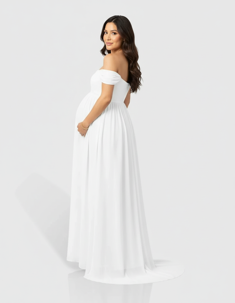 Maternity model in a white off-shoulder laced flowing maxi dress, gently holding her baby bump.