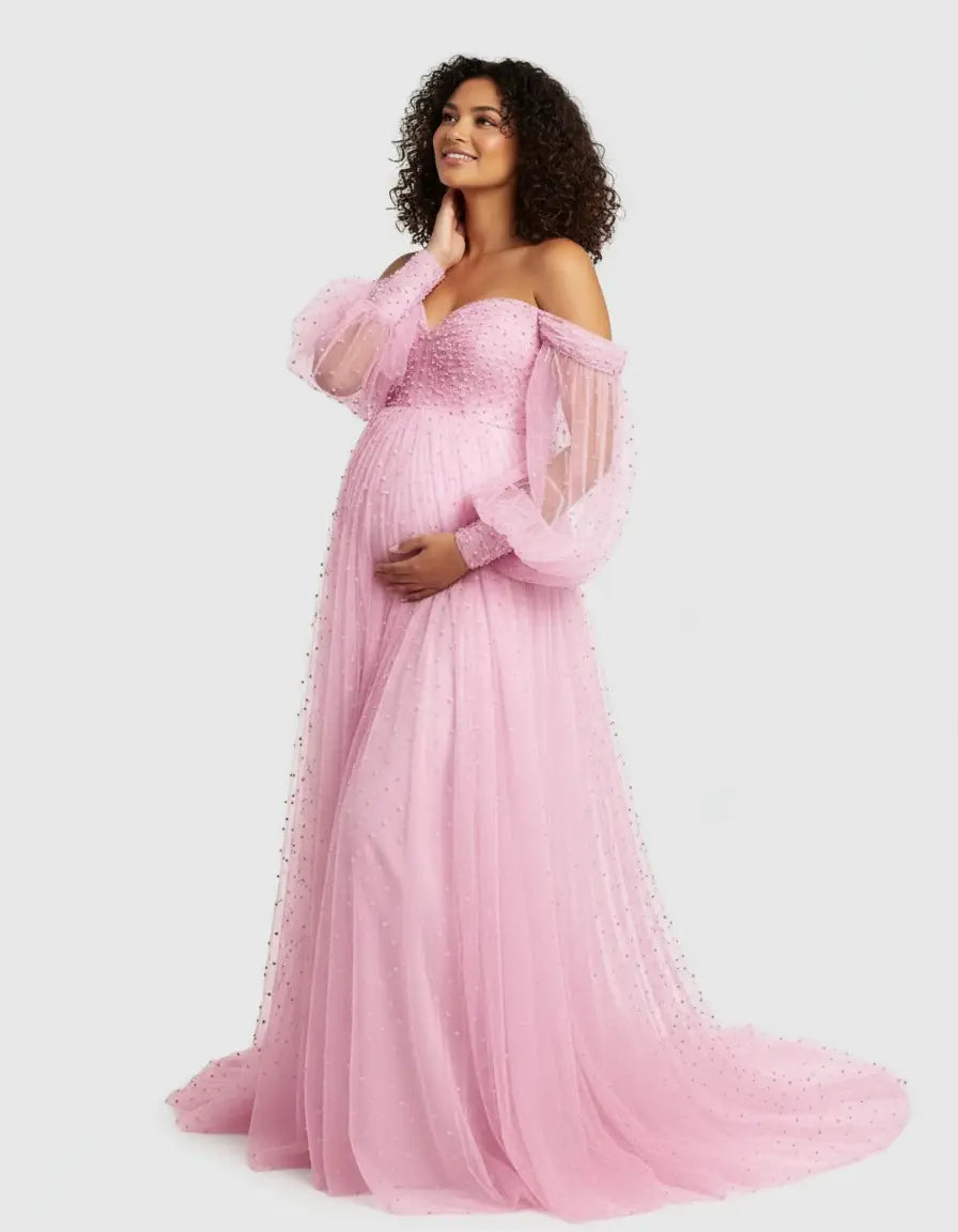 Smiling pregnant woman in a pink off-shoulder tulle train maternity gown with embellished sleeves.