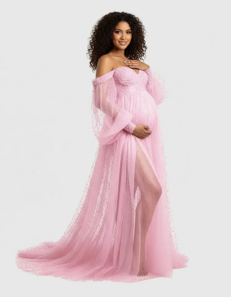Pregnant woman in a pink off-shoulder tulle gown with long sleeves, a train, and subtle embellishments.