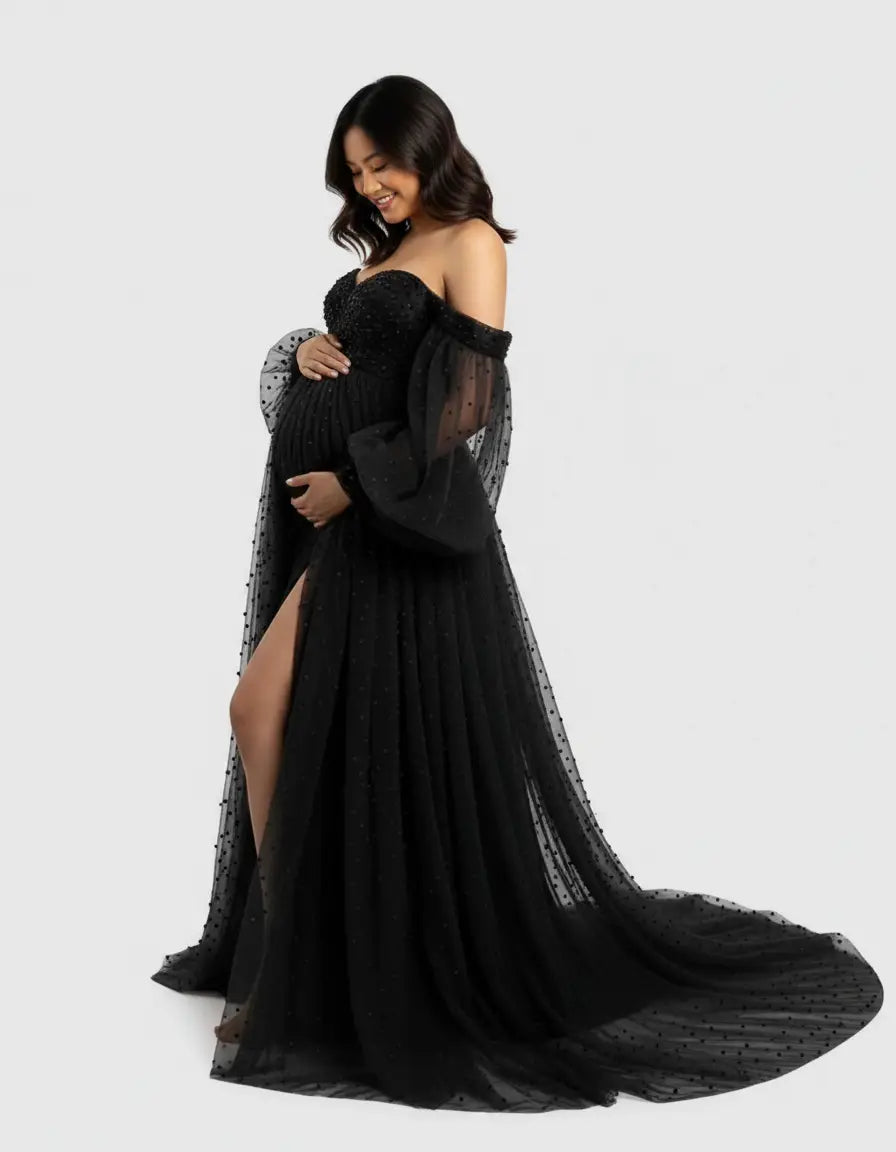 Smiling pregnant woman in a black off-shoulder tulle train maternity gown with polka dots and a high slit.