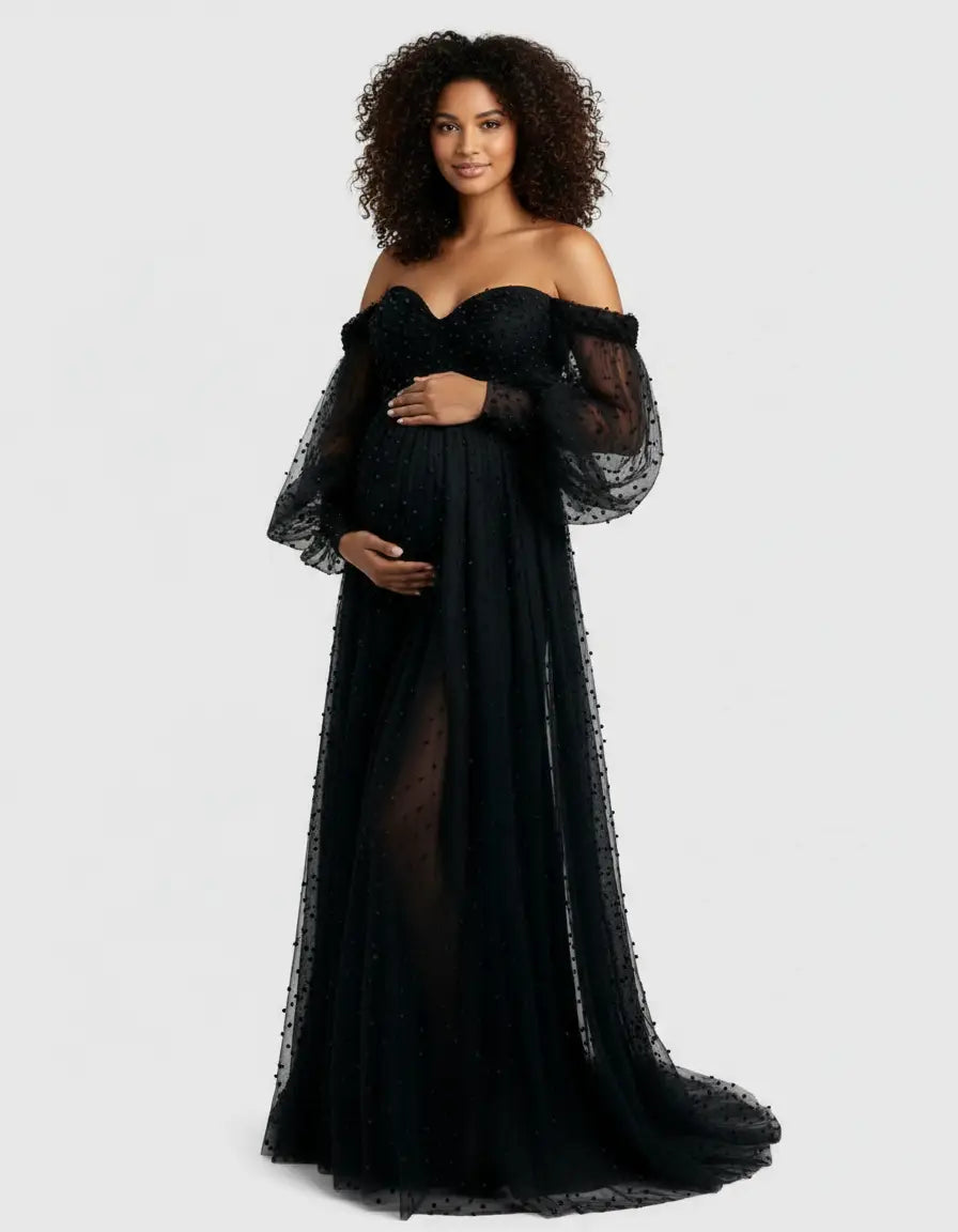 Pregnant woman in a black off-shoulder tulle train maternity gown with polka dots and long sleeves.