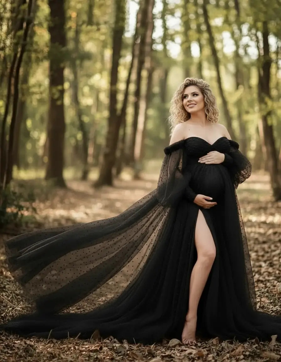Pregnant woman in a black off-shoulder tulle train maternity gown with polka dots, standing in a forest.
