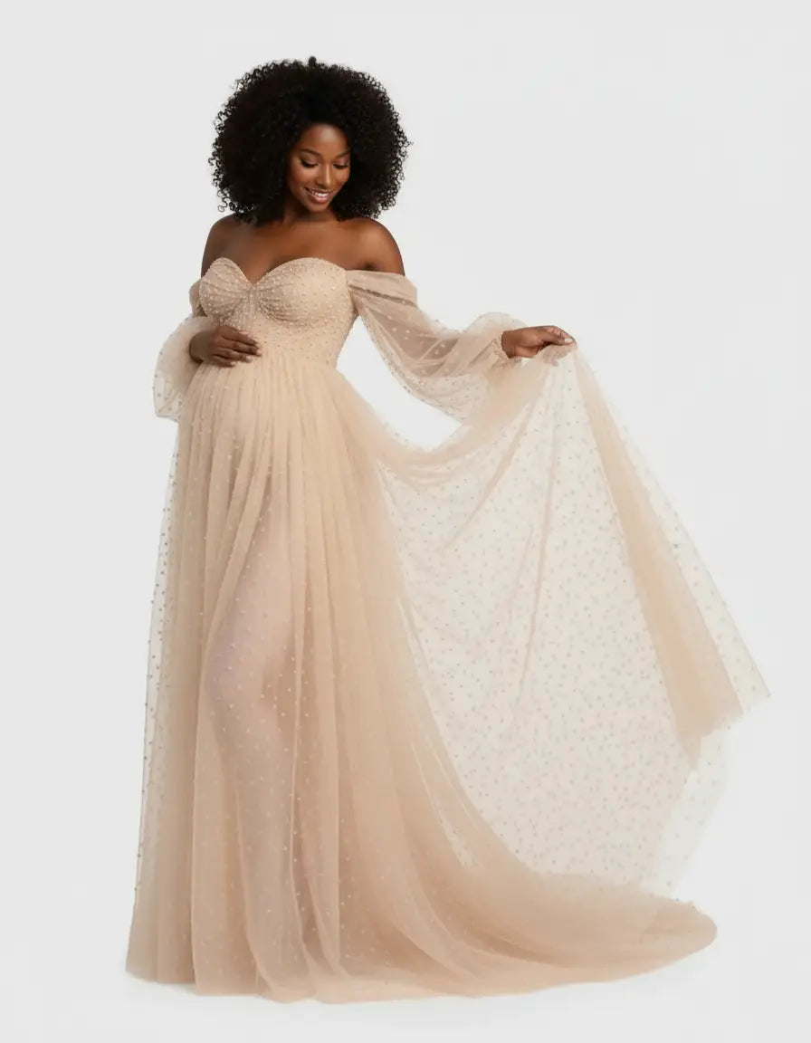 Smiling pregnant woman in a nude off-shoulder tulle train maternity gown with delicate pearl embellishments.