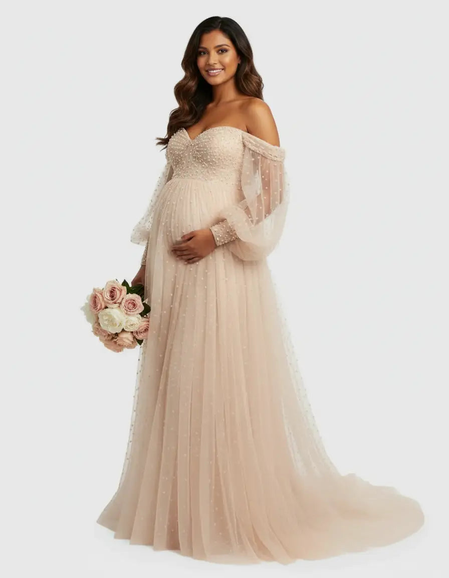 Smiling pregnant woman in an off-shoulder, light pink tulle maternity gown with pearl details and a train.