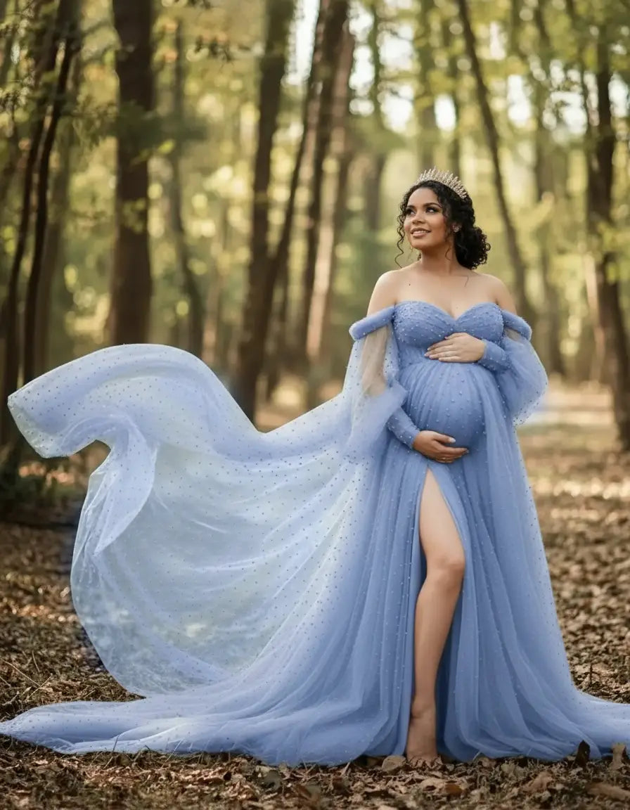 Pregnant woman in a blue off-shoulder tulle gown with a long train and thigh-high slit, wearing a crown in a forest.