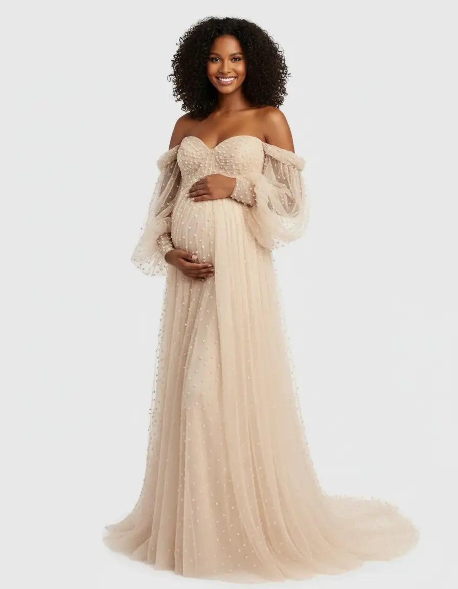 Smiling pregnant woman in an off-shoulder, pearl-embellished beige tulle maternity gown with a train.