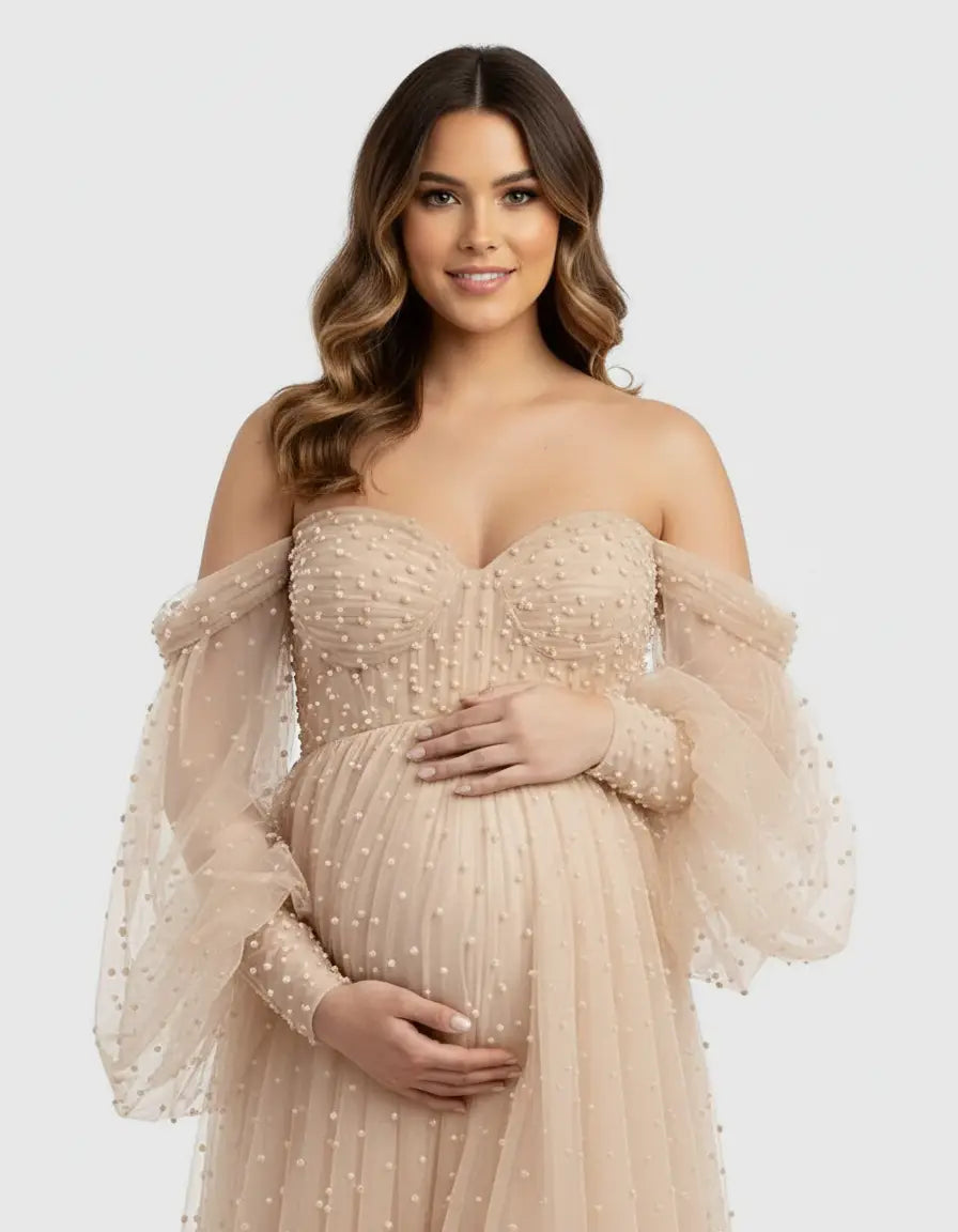 Off-shoulder tulle train maternity gown in nude with pearl embellishments, worn by a smiling pregnant woman.