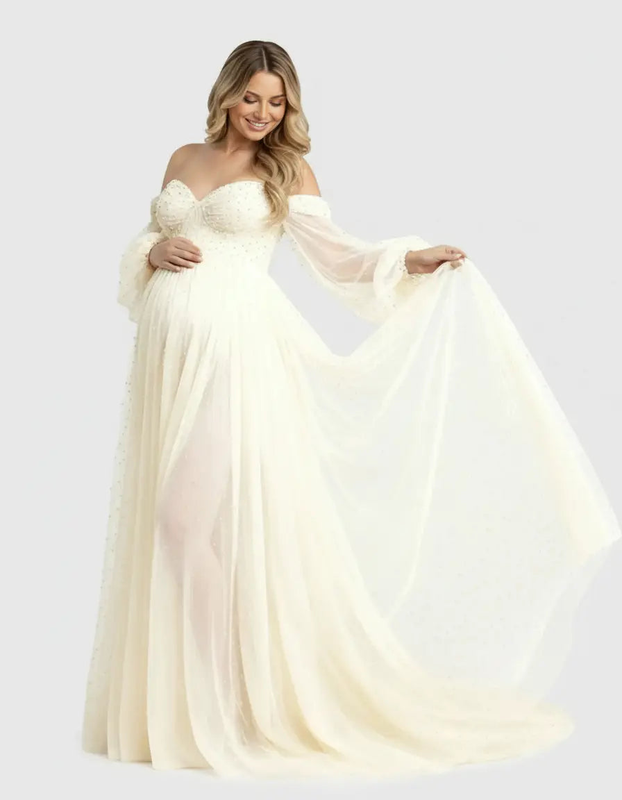 Blonde pregnant woman in an off-shoulder ivory tulle maternity gown with a sweetheart neckline and long sleeves.