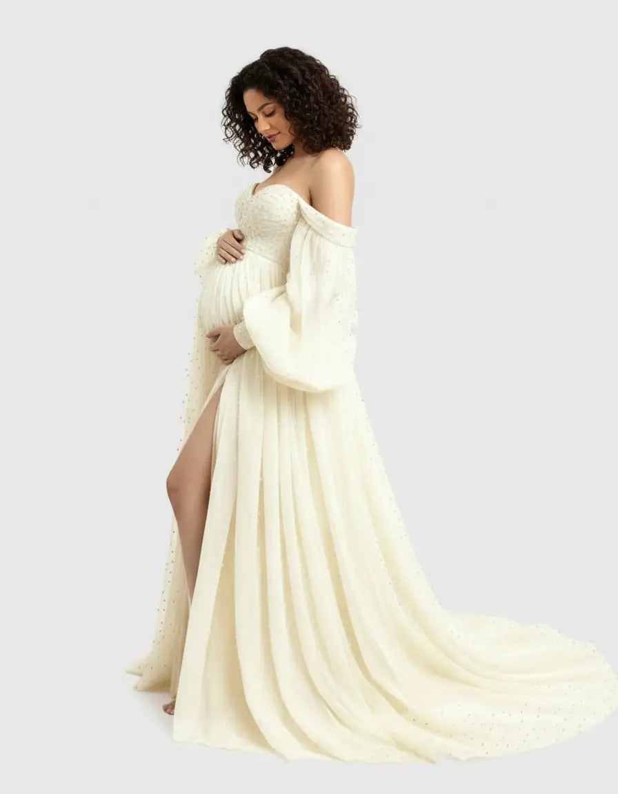 Maternity gown: off-shoulder, long-sleeved, ivory tulle with train and high slit, worn by a pregnant woman.