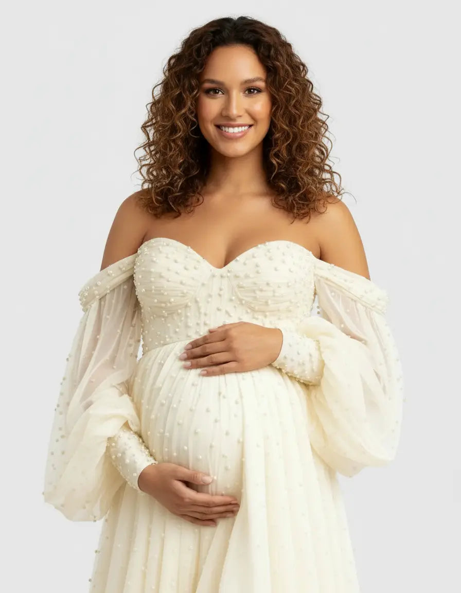 Smiling pregnant woman in an off-shoulder ivory tulle gown with pearl embellishments.