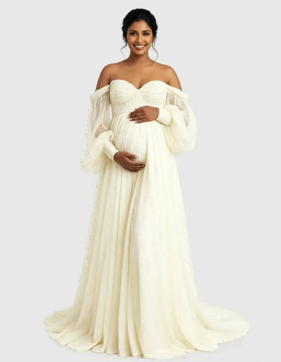 Smiling pregnant woman in an off-shoulder ivory tulle train maternity gown with long, sheer, dotted sleeves.