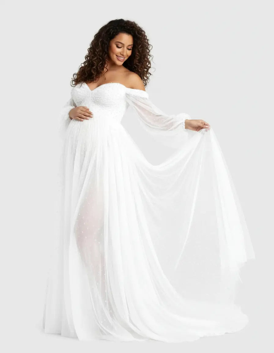Smiling pregnant woman in a white off-shoulder tulle train maternity gown with long sleeves.