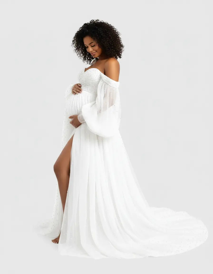 Smiling pregnant woman in a white off-shoulder tulle train maternity gown with a high slit.