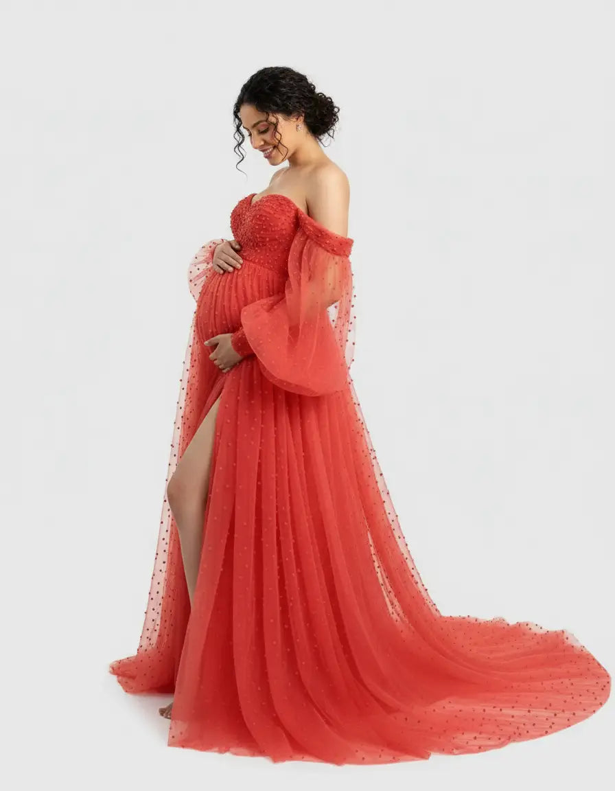Pregnant woman in an off-shoulder, red tulle gown with a train, long sleeves, and high slit.