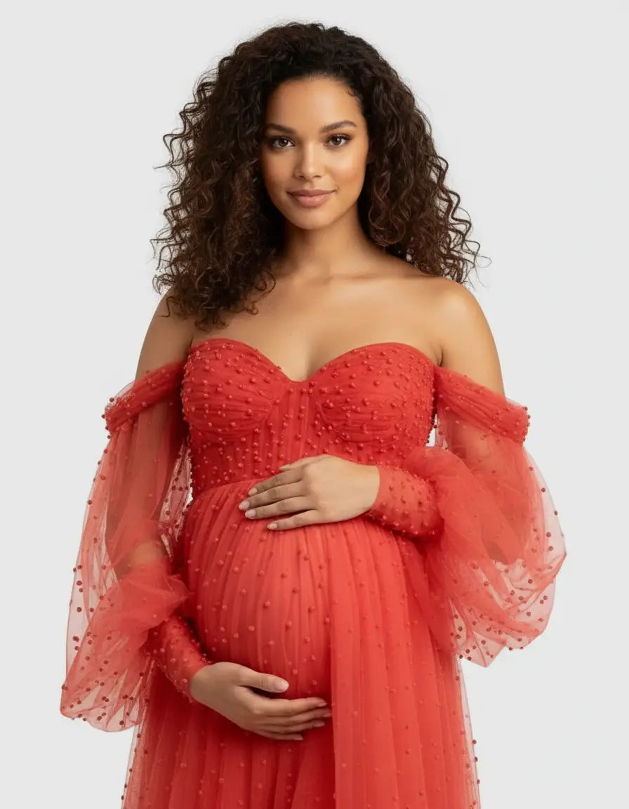Pregnant woman in an off-shoulder red tulle maternity gown with textured polka dots and long puff sleeves.