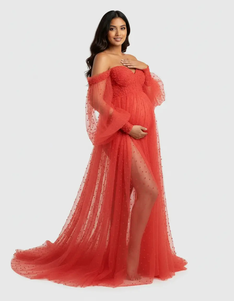 Red off-shoulder tulle train maternity gown with long sheer sleeves and polka dot embellishments.