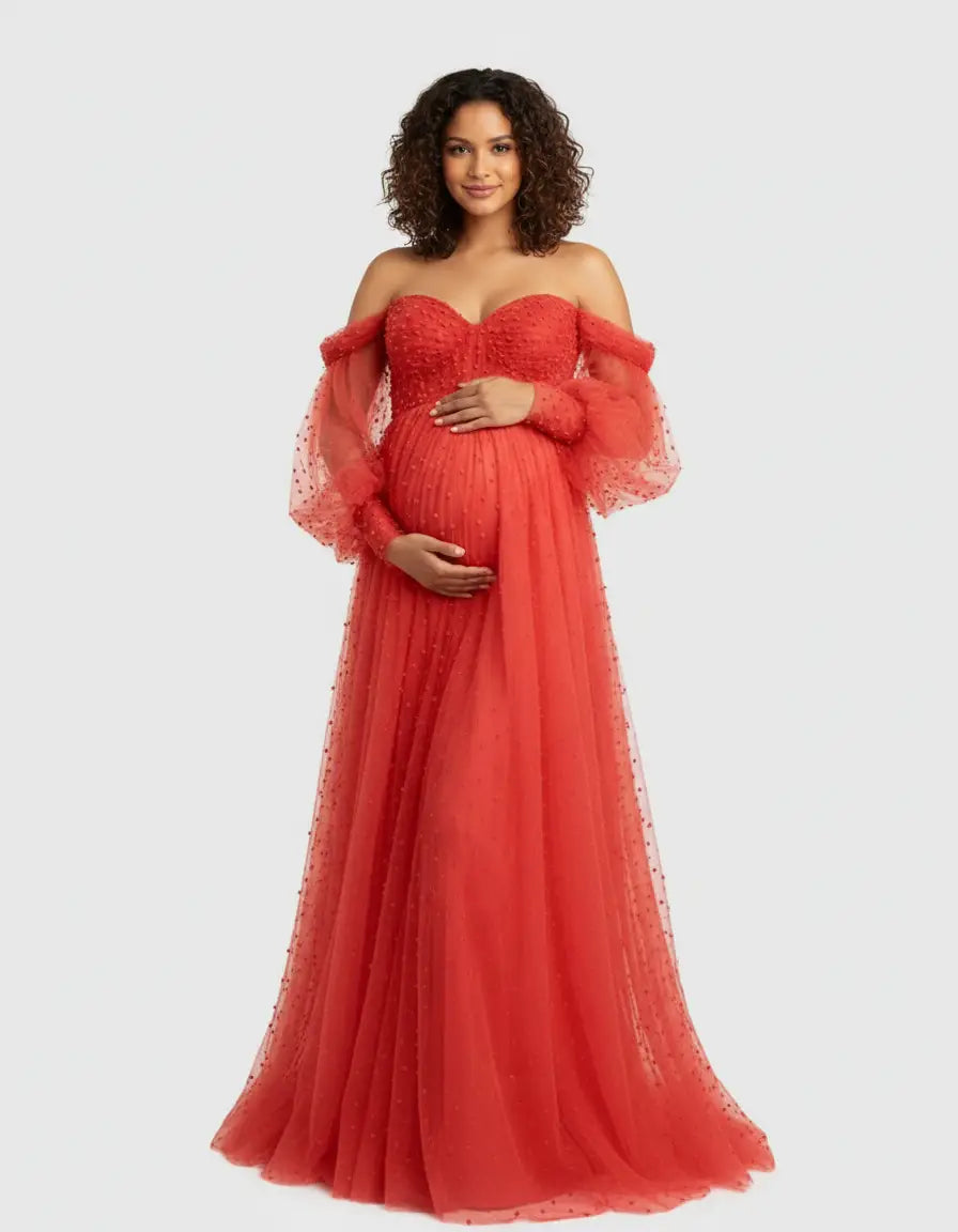 Pregnant woman in a red off-shoulder tulle train maternity gown with puffed sleeves and pearl details.