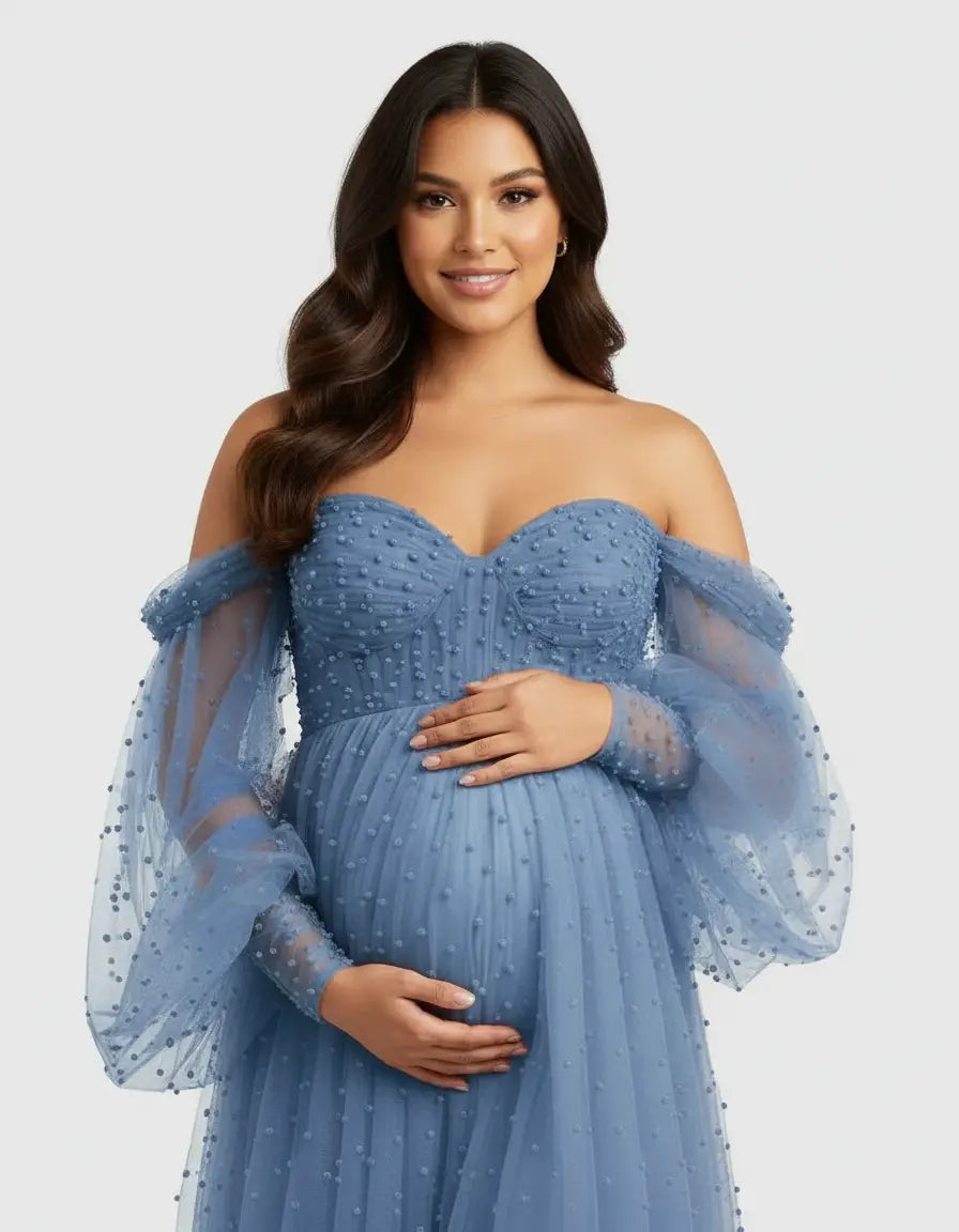 Smiling pregnant woman in a blue off-shoulder tulle gown with beaded details and long balloon sleeves.