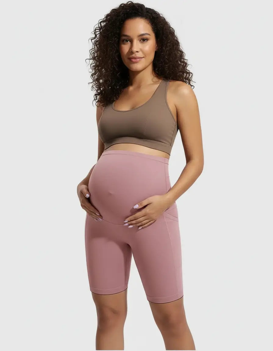 Pregnant woman in pink over-belly maternity bike shorts with pockets and a brown sports bra.