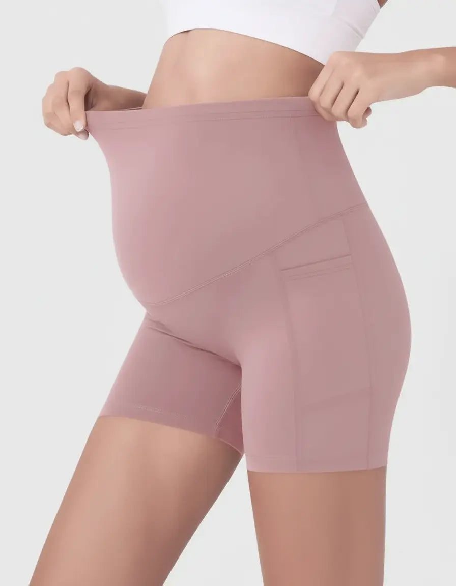 Maternity bike shorts in dusty rose, featuring an over-belly design and side pockets, modeled on a pregnant woman.