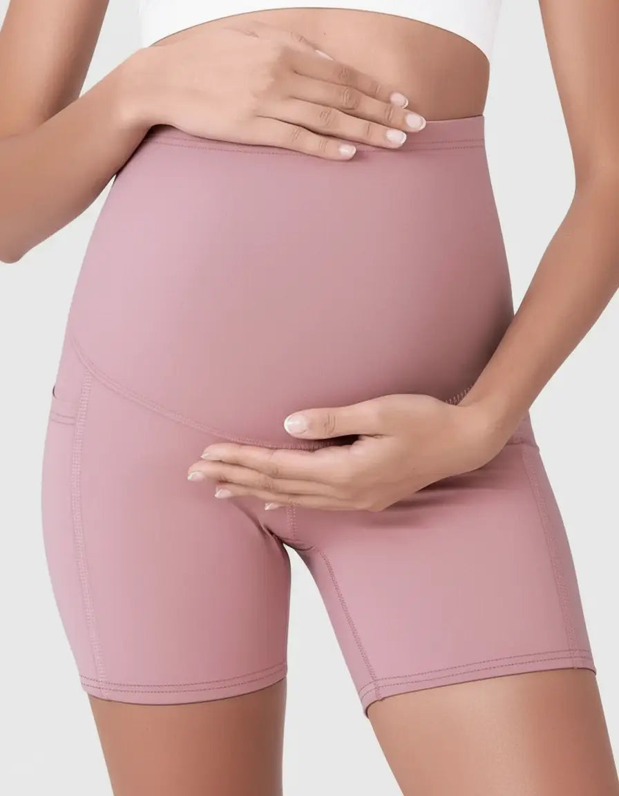 Maternity Over Belly Bike Short in dusty rose with side pockets, worn by a pregnant woman.