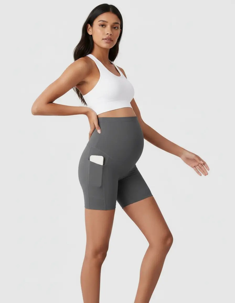 Pregnant woman in gray over-belly maternity bike shorts with side pockets and a white sports bra.