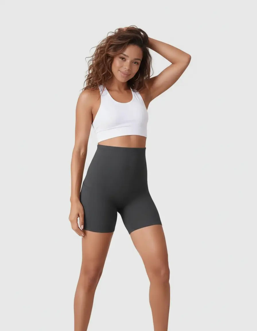 Smiling woman in dark gray over-belly maternity bike shorts with pockets and a white sports bra.