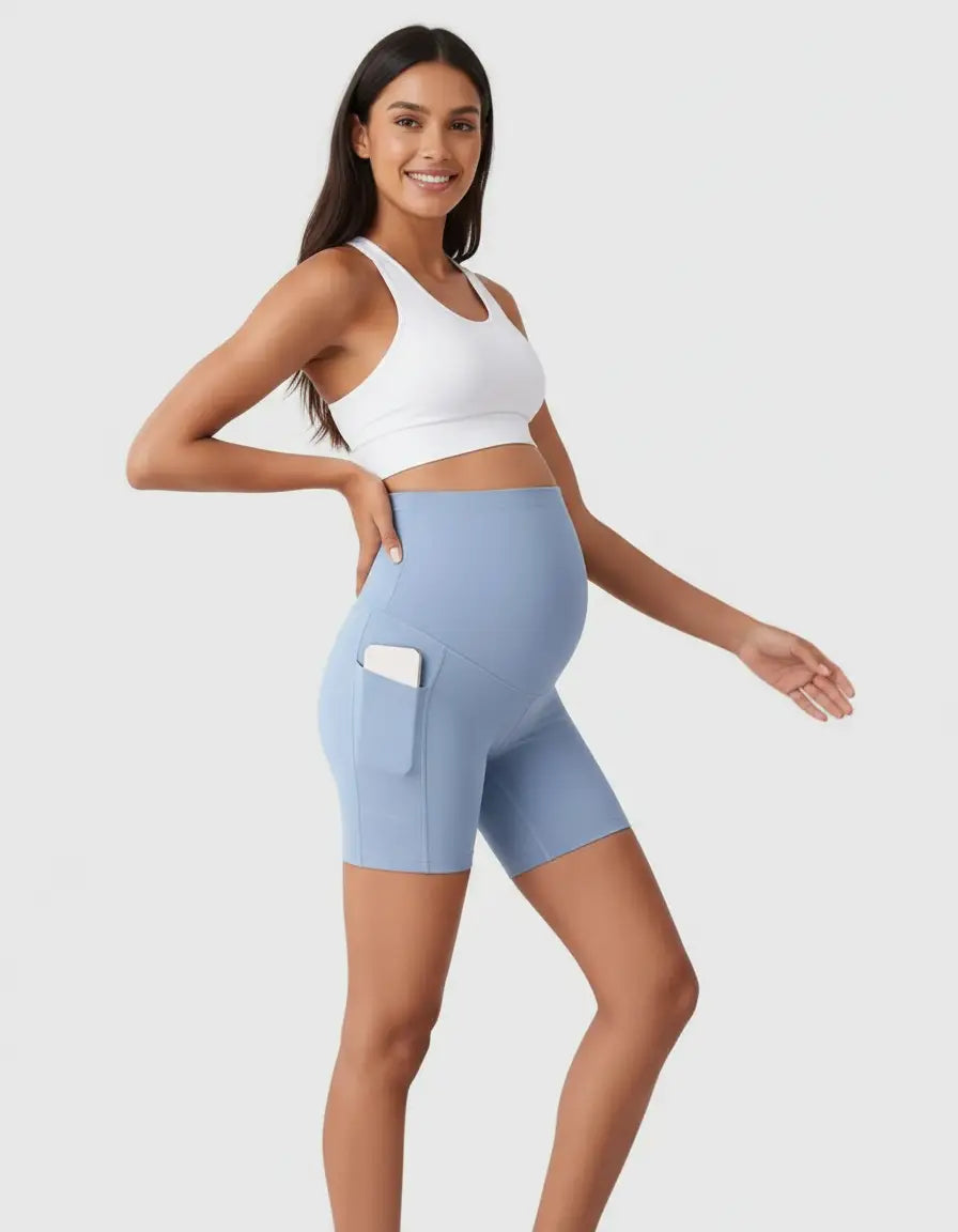 Smiling pregnant woman wearing light blue over-belly maternity bike shorts with a phone in the side pocket.
