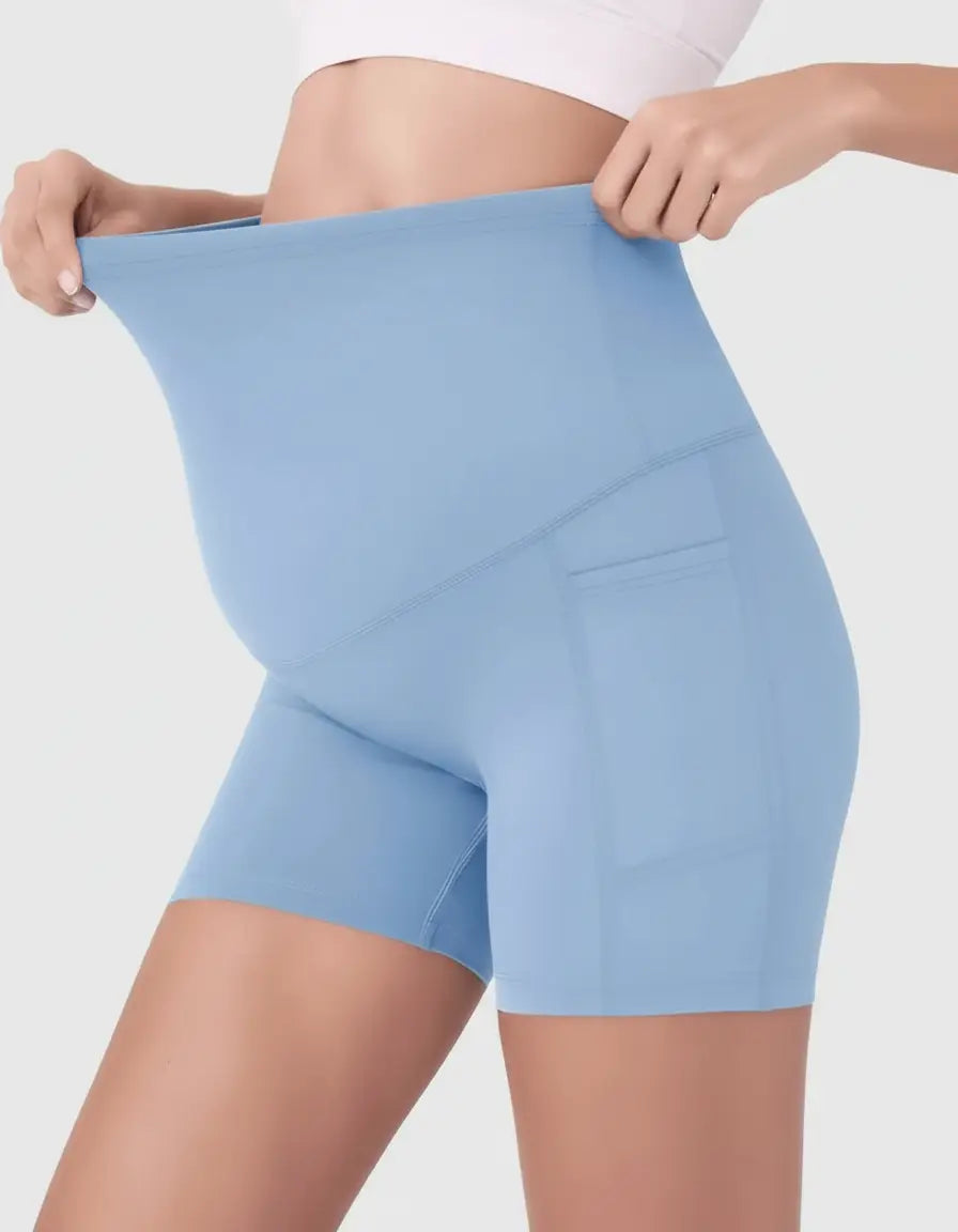 Light blue over-belly maternity bike shorts with side pockets, shown on a pregnant model.
