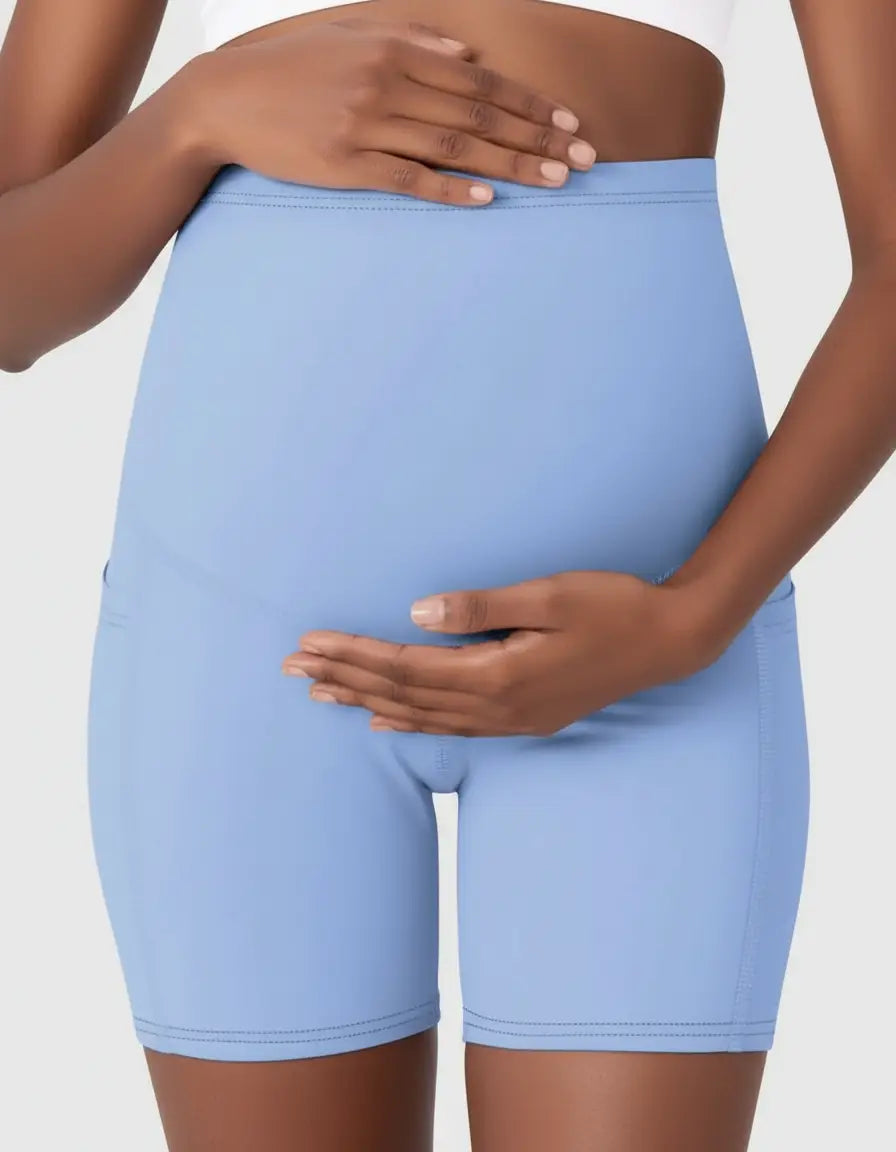 Pregnant woman wearing light blue over-belly maternity bike shorts with pockets.