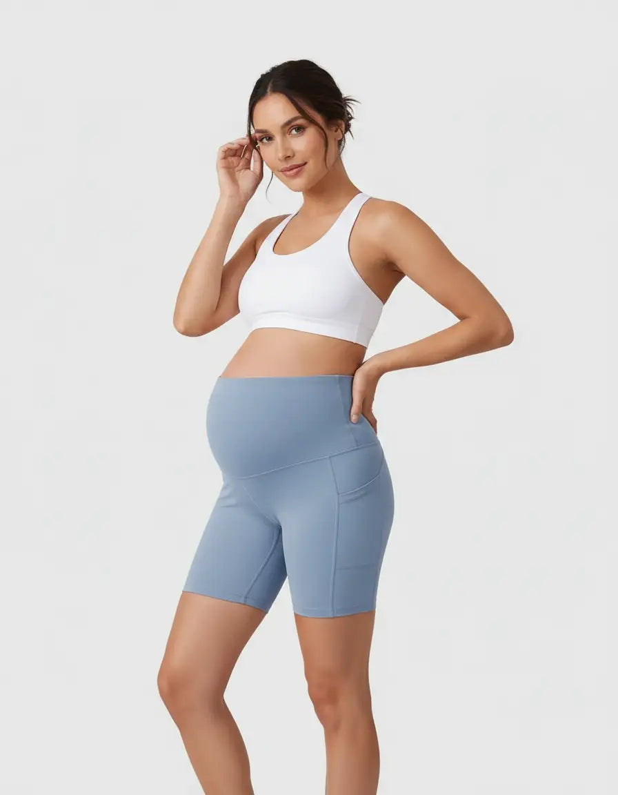 Pregnant woman in blue over-belly maternity bike shorts with side pockets and a white sports bra.