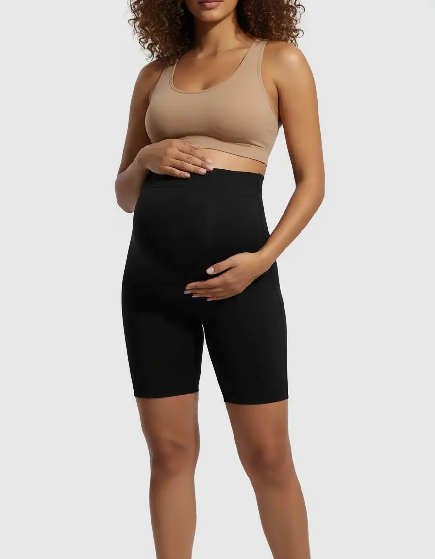Pregnant woman wearing black over-belly maternity bike shorts with pockets and a nude bra.