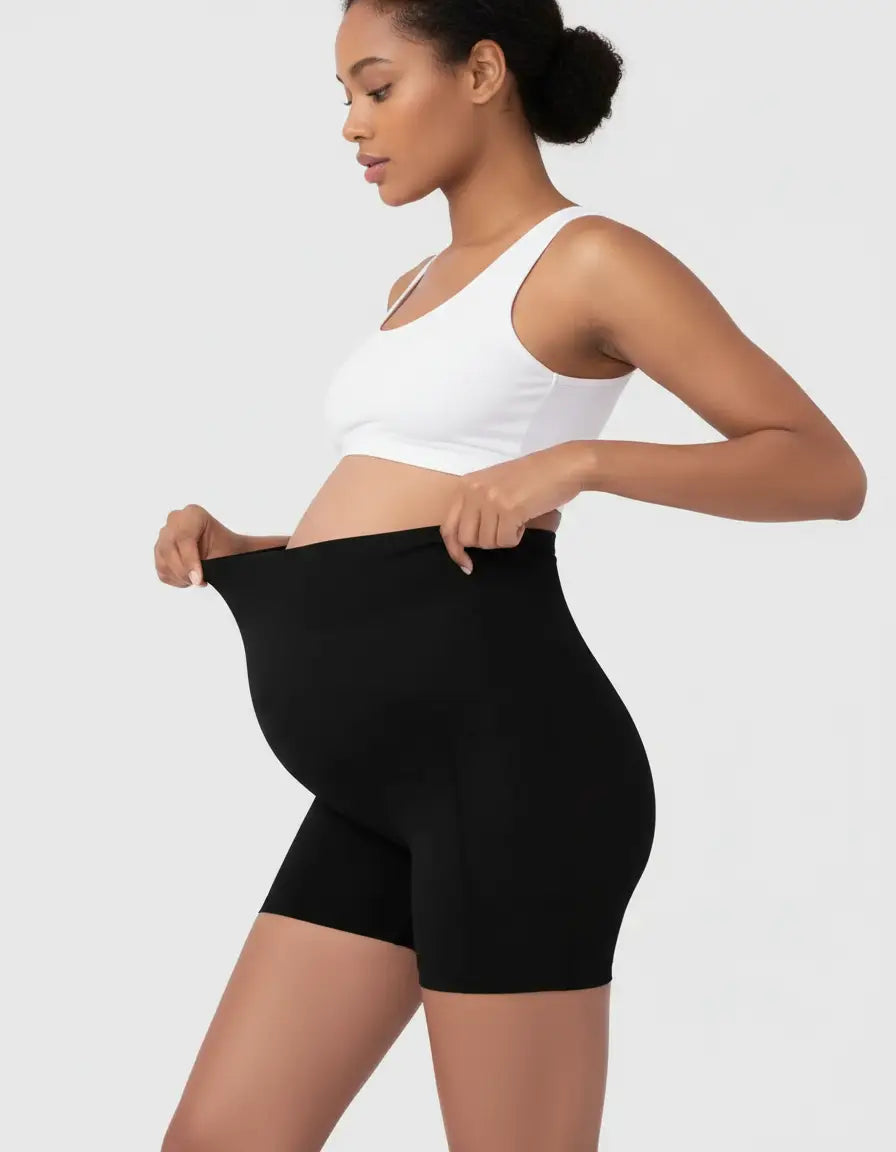 Pregnant woman in black over-belly maternity bike shorts with pockets, white bra.