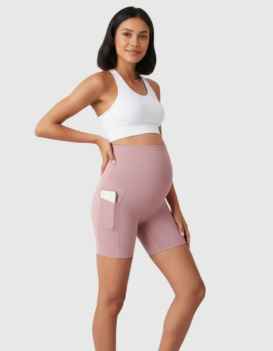 Pregnant woman in pink over-belly maternity bike shorts with side pockets and a white sports bra.