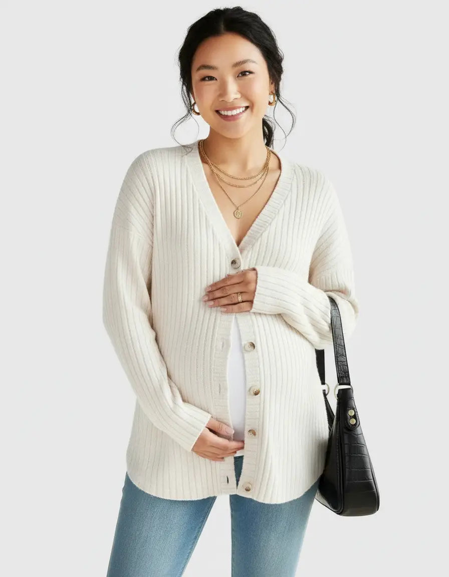 Smiling pregnant woman in a cream ribbed button-front drop shoulder maternity cardigan, light wash jeans, and gold jewelry.