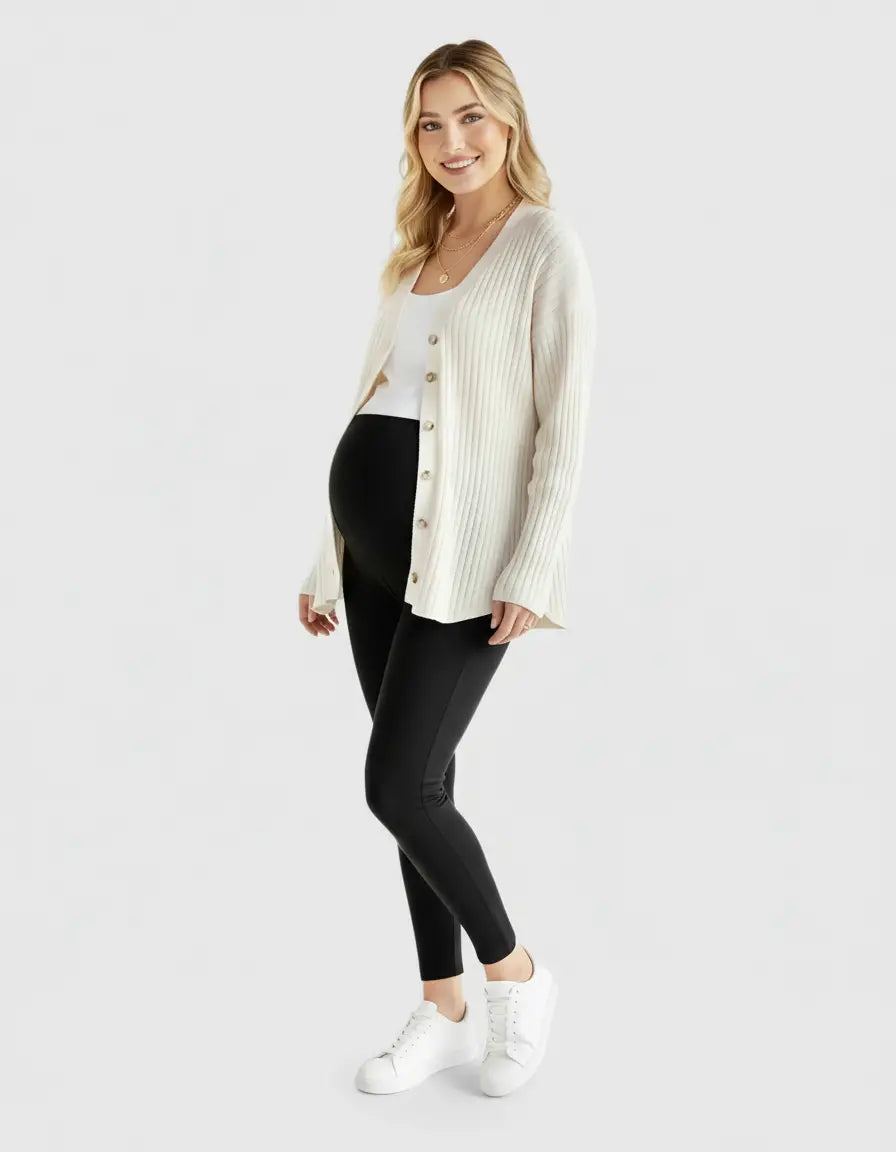 Smiling pregnant woman in a cream ribbed button-front drop shoulder maternity top, white tank, and black leggings.