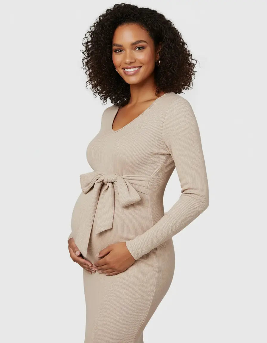 Smiling pregnant woman in a beige ribbed knit bodycon maternity midi dress with a front tie bow.