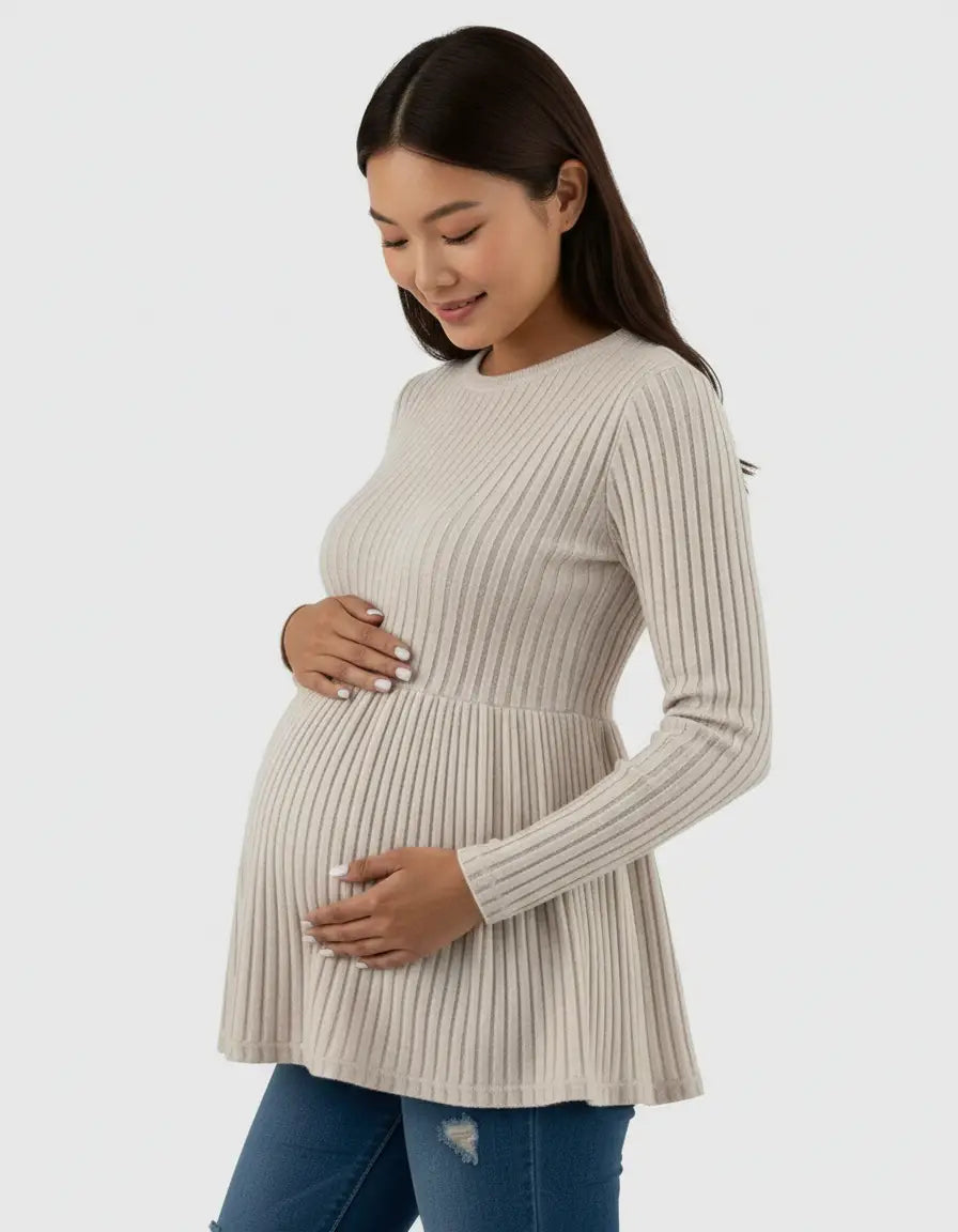 Smiling pregnant woman in a beige ribbed knit maternity top with a ruffle hem and long sleeves.