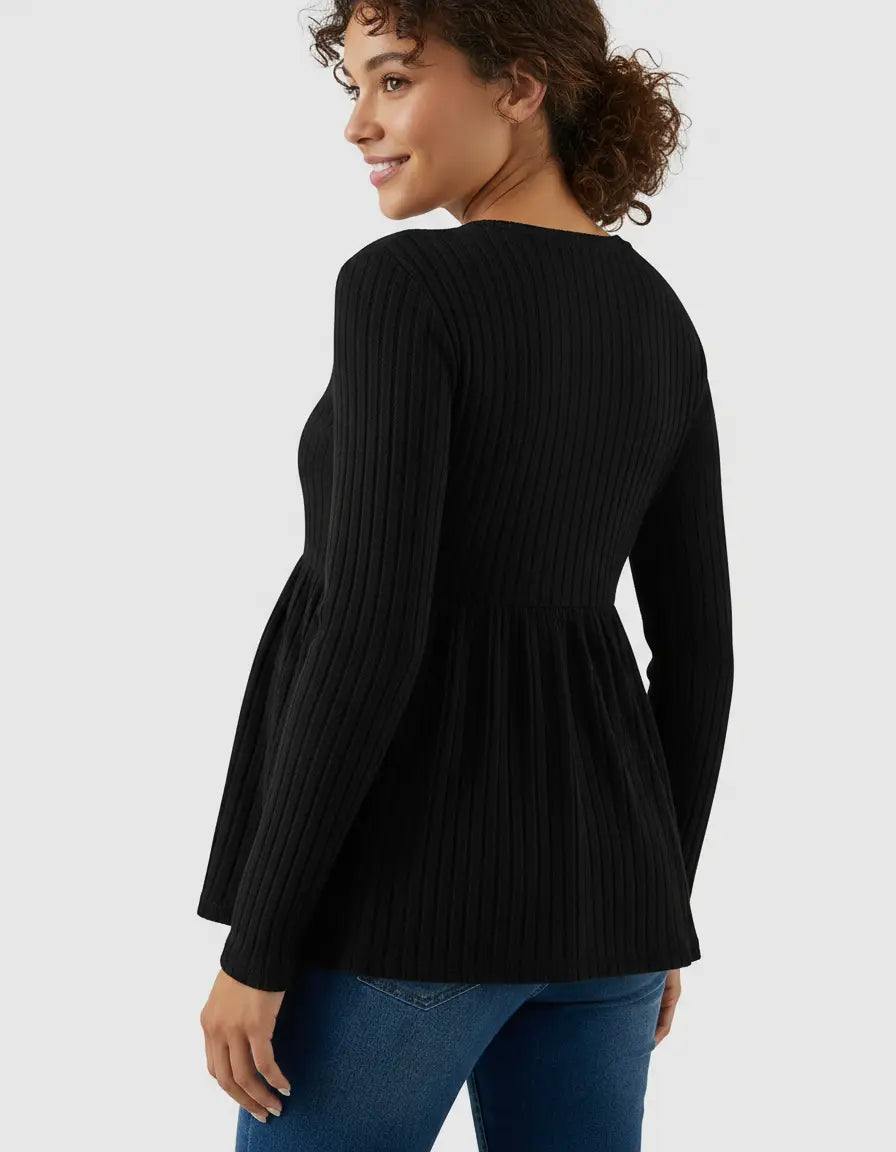 Smiling woman in a black ribbed knit long-sleeve maternity top with a ruffle hem, paired with jeans.