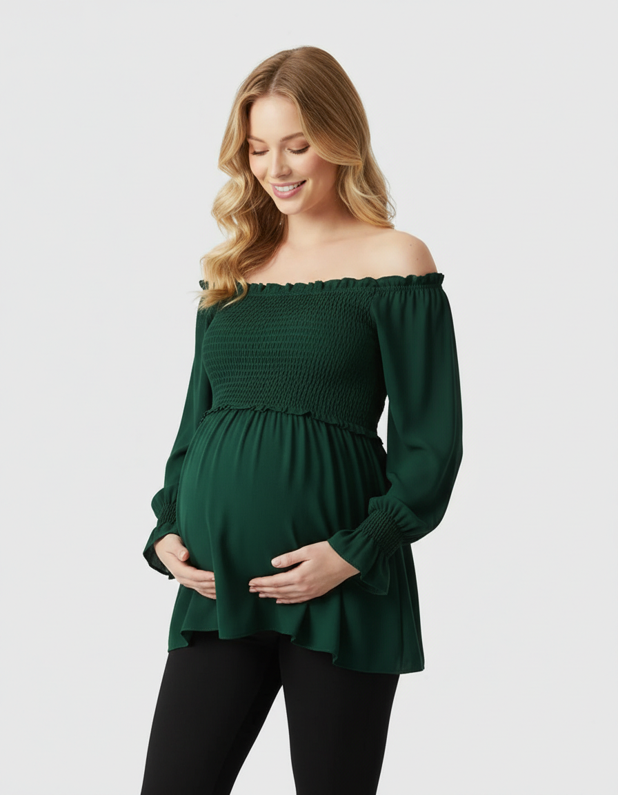 Smiling pregnant woman in a dark green ruched off-shoulder maternity top with long sleeves, holding her belly.