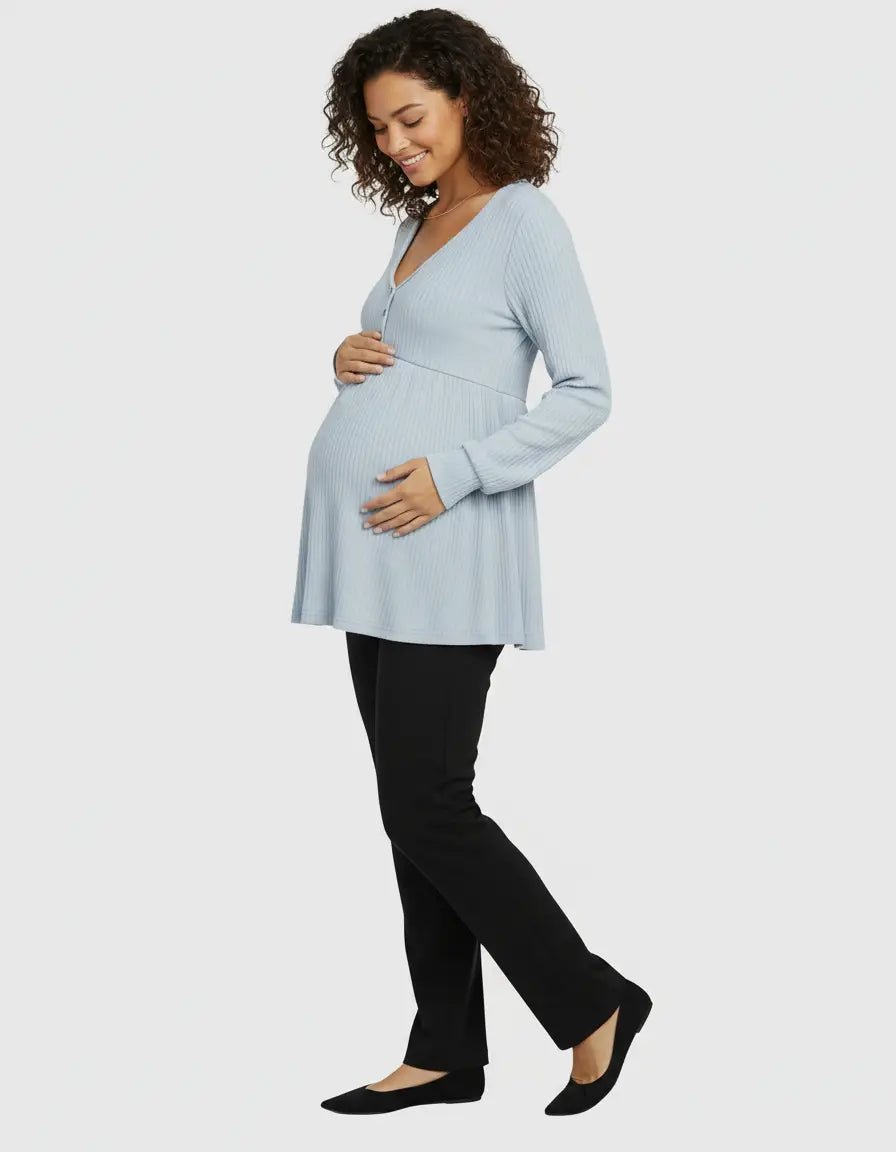 Smiling pregnant woman in a light blue ribbed ruffled V-neck maternity top and black pants.