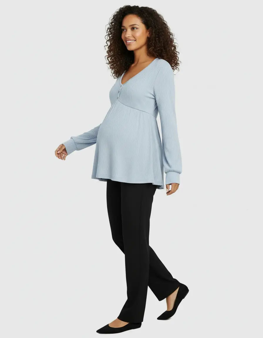 Smiling pregnant woman in a light blue ribbed V-neck maternity top with long sleeves and black pants.