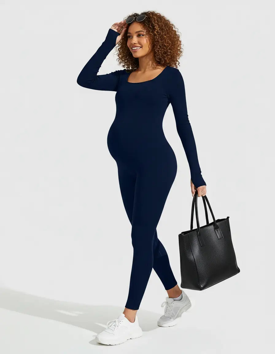 Smiling pregnant woman in a navy seamless ankle-length maternity bodysuit, holding a black tote bag.