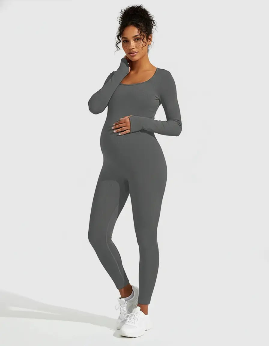 Pregnant woman in a charcoal gray ribbed seamless ankle-length maternity bodysuit with long sleeves and a scoop neck.