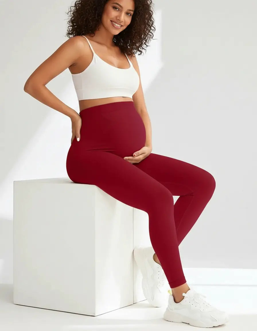Smiling pregnant woman wearing high-waisted, full-length soft-stretch burgundy maternity leggings and a white crop top.