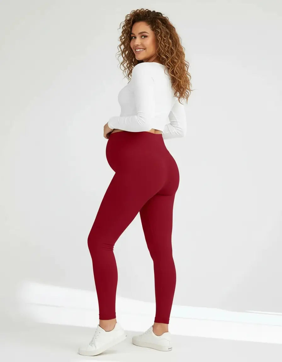 Smiling pregnant woman wearing full-length, soft-stretch, high-waisted red maternity leggings and a white crop top.