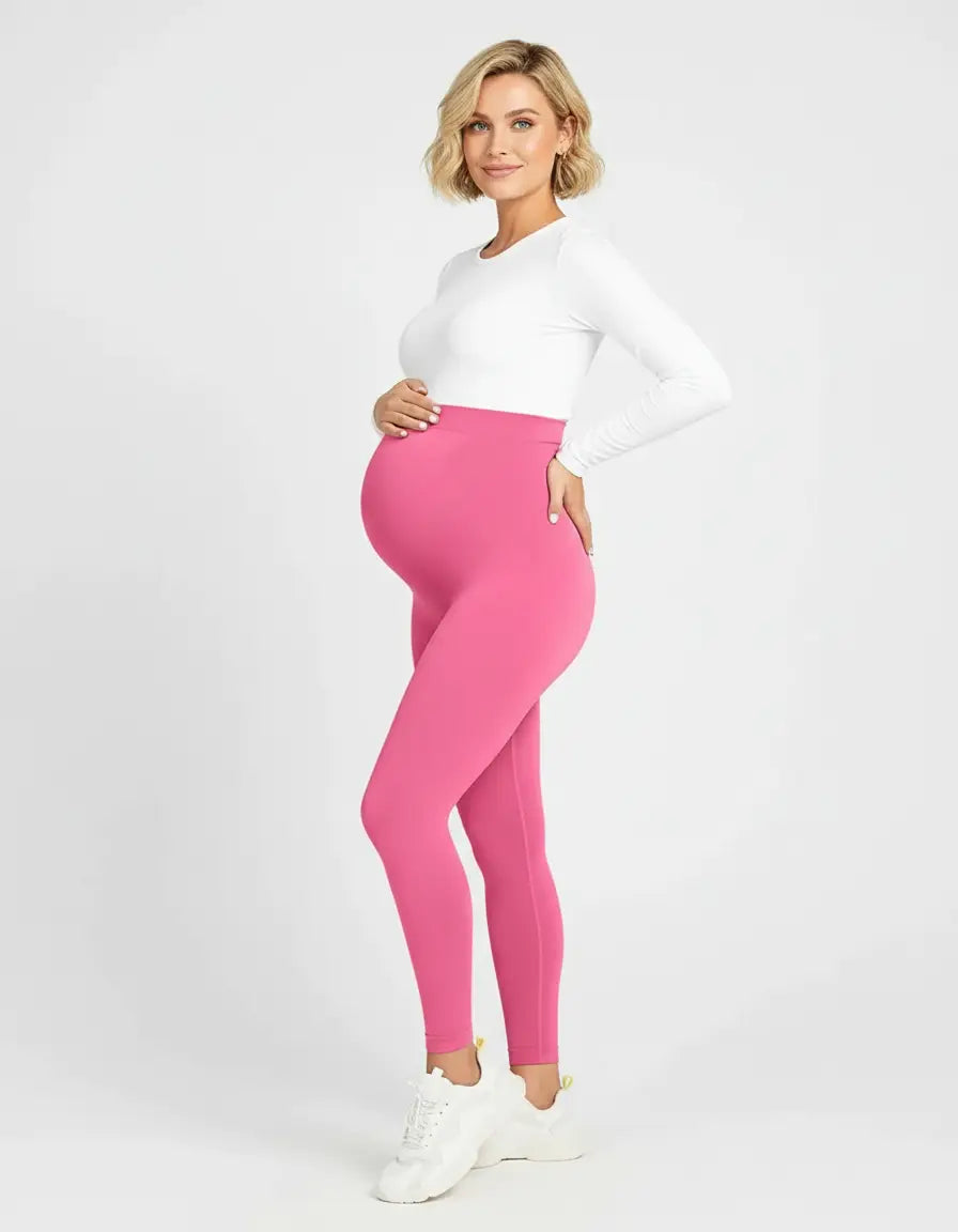 Smiling pregnant woman in pink soft-stretch full-length maternity leggings and a white long-sleeve top.