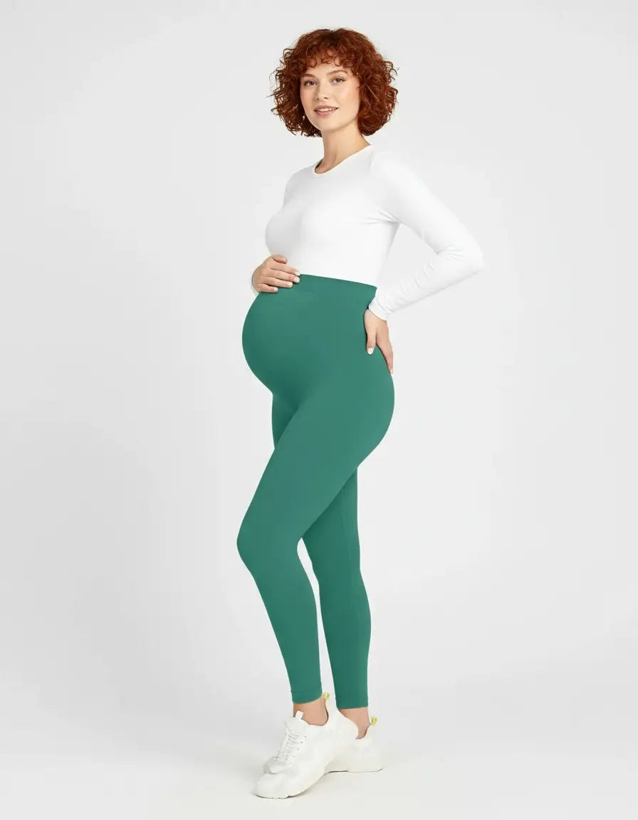 Pregnant woman in soft-stretch, full-length teal maternity leggings and a white long-sleeve top.