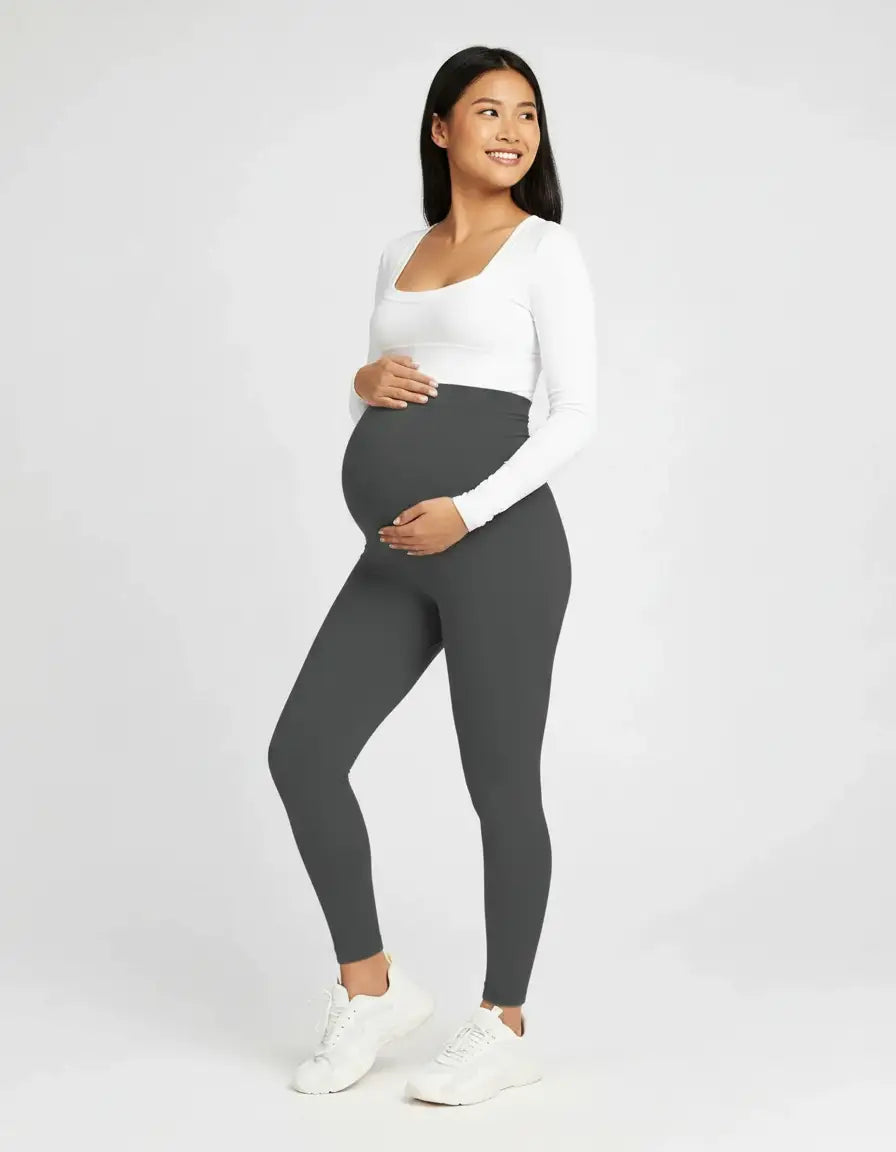 Smiling pregnant woman in dark gray soft-stretch full-length maternity leggings and a white top.